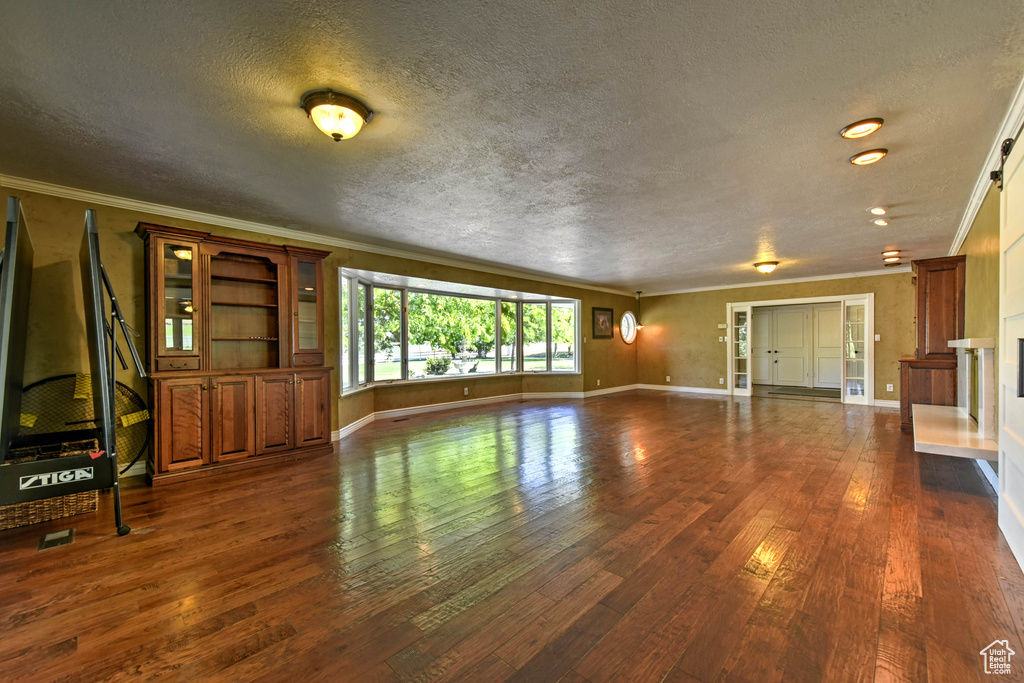 Unfurnished living room with a textured ceiling, dark hardwood / wood-style flooring, and ornamental molding