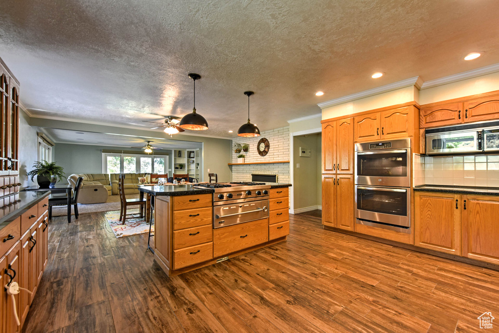 Kitchen featuring ceiling fan, stainless steel appliances, crown molding, a center island, and dark hardwood / wood-style floors