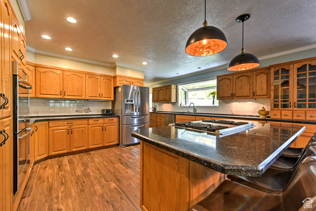 Kitchen featuring hardwood / wood-style flooring, stainless steel appliances, tasteful backsplash, and pendant lighting