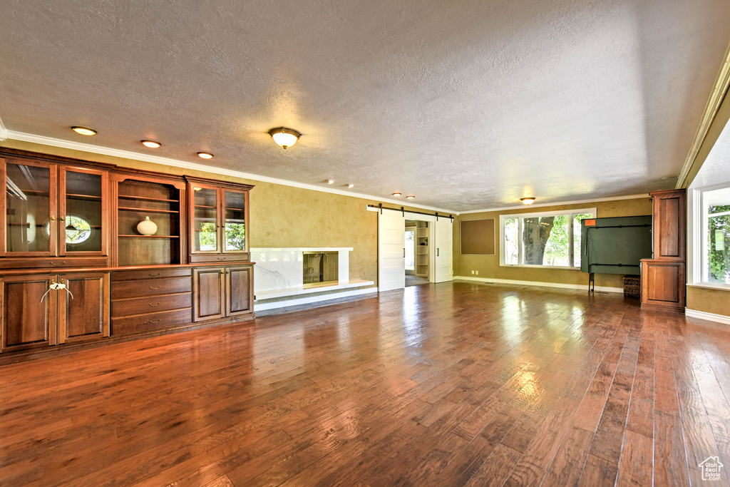 Unfurnished living room featuring ornamental molding, a barn door, a textured ceiling, and dark wood-type flooring