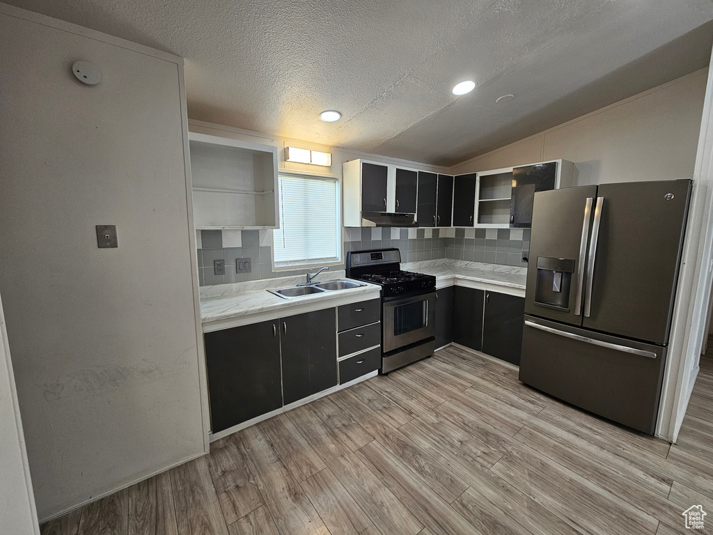 Kitchen with stainless steel appliances, vaulted ceiling, sink, light hardwood / wood-style floors, and decorative backsplash