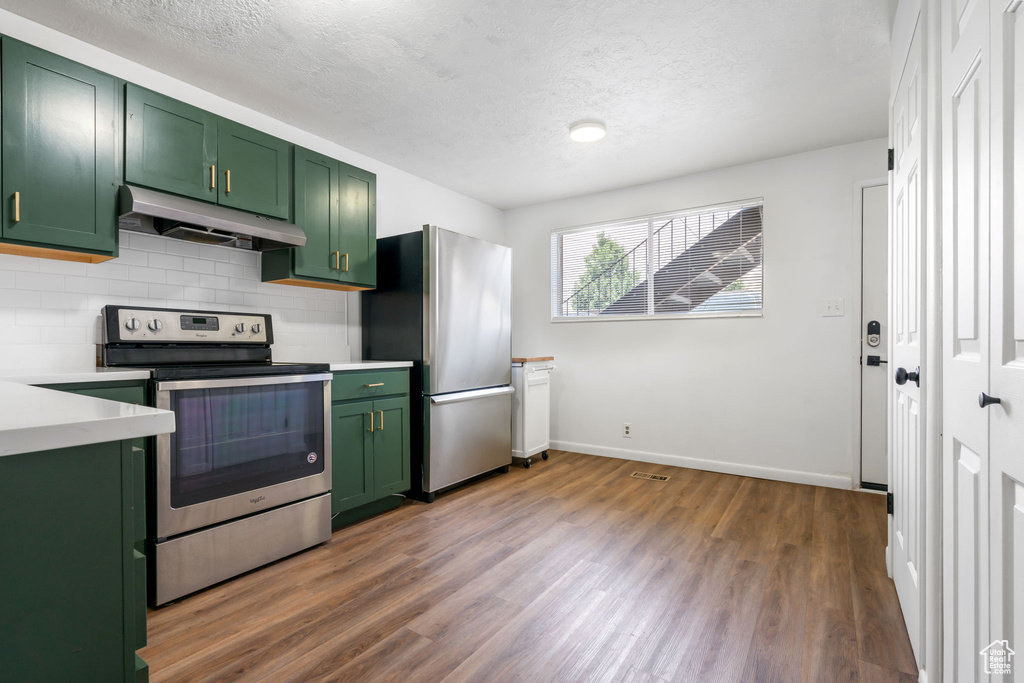 Kitchen with stainless steel appliances, tasteful backsplash, green cabinets, and dark wood-type flooring