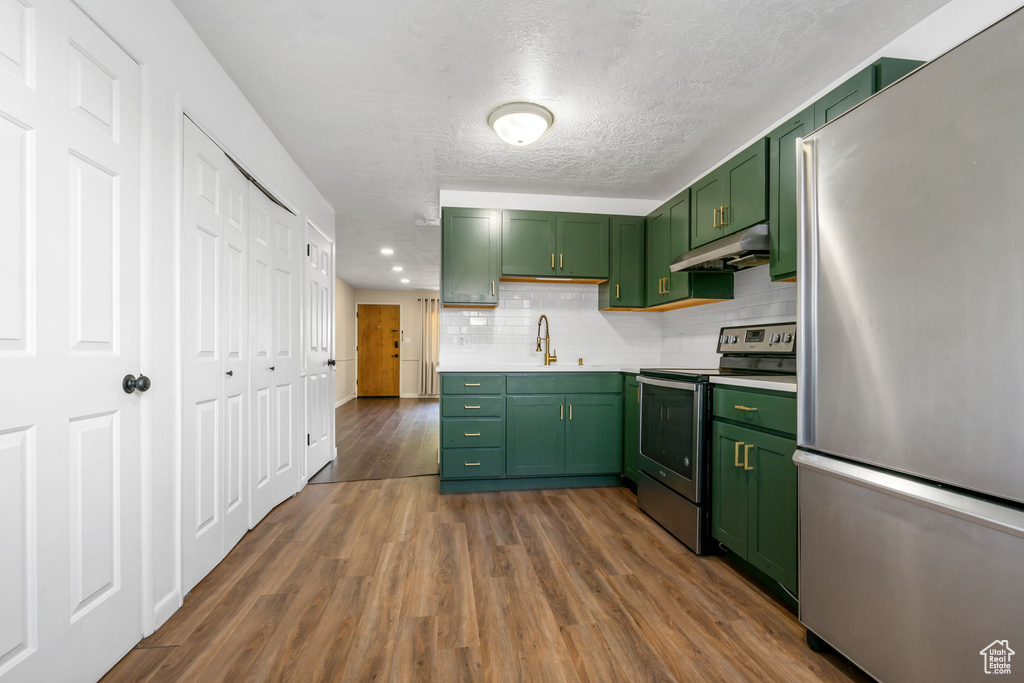 Kitchen with hardwood / wood-style floors, green cabinets, decorative backsplash, and appliances with stainless steel finishes