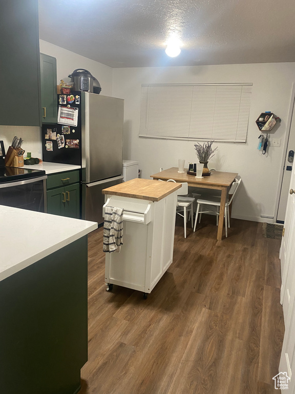 Kitchen featuring a textured ceiling, dark hardwood / wood-style flooring, green cabinetry, appliances with stainless steel finishes, and washer / dryer