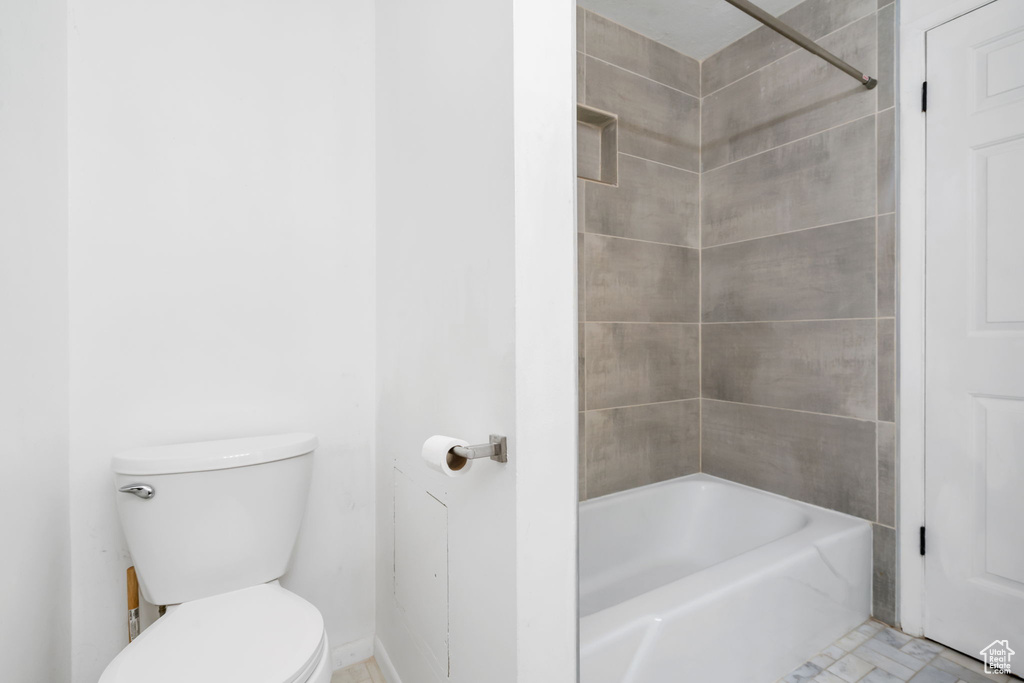 Bathroom with tile patterned floors, tiled shower / bath combo, and toilet