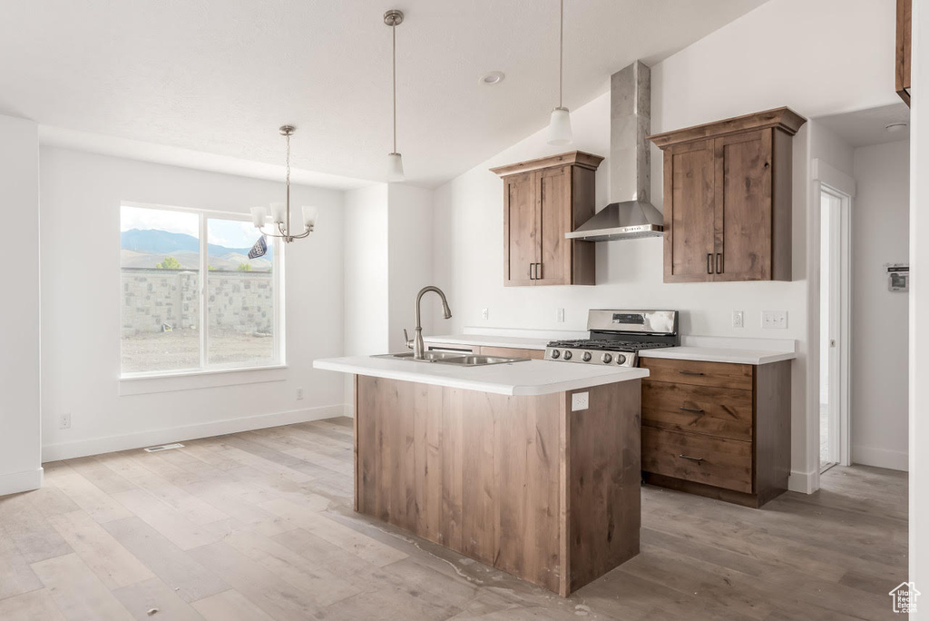 Kitchen with a kitchen island with sink, exhaust hood, stove, and light wood-type flooring