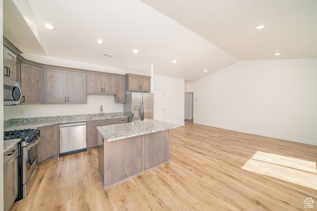 Kitchen with sink, a center island, light stone counters, light hardwood / wood-style floors, and appliances with stainless steel finishes