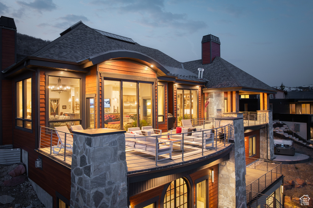 Back of property featuring a shingled roof, stone siding, a balcony, and a chimney