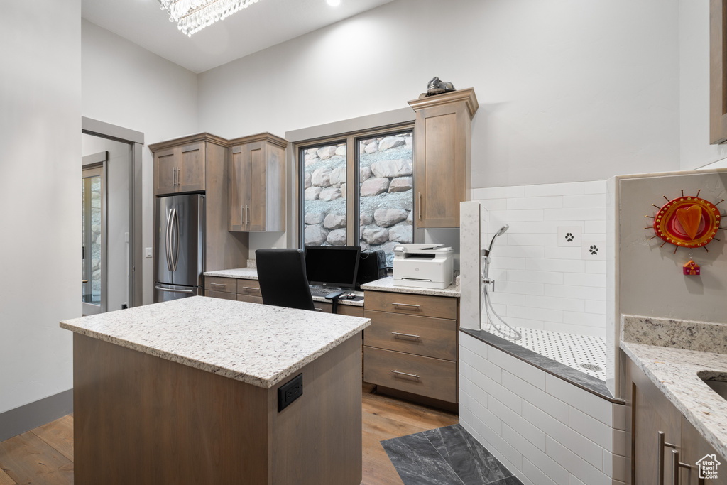 Kitchen with light stone countertops, light wood finished floors, a center island, and freestanding refrigerator