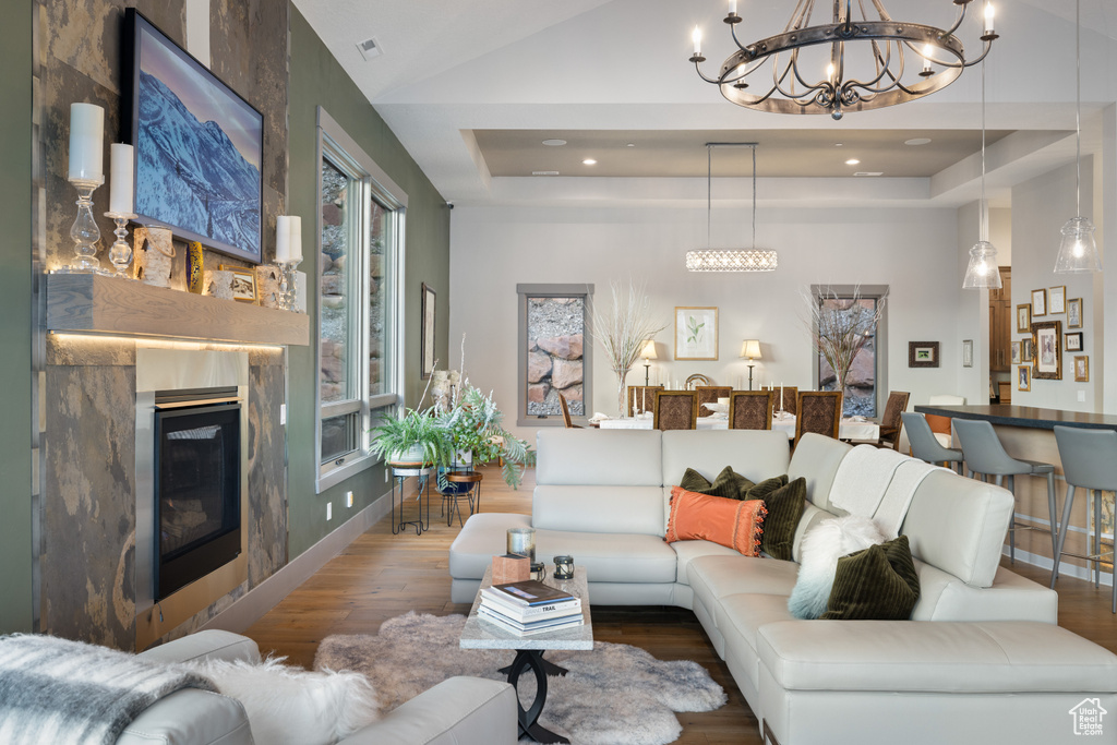 Living area featuring a tray ceiling, a glass covered fireplace, visible vents, wood finished floors, and a notable chandelier