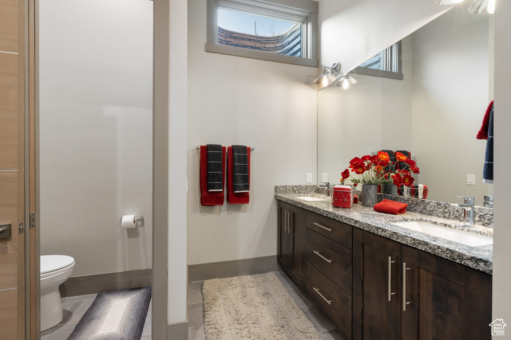Full bath with toilet, double vanity, a sink, and tile patterned flooring