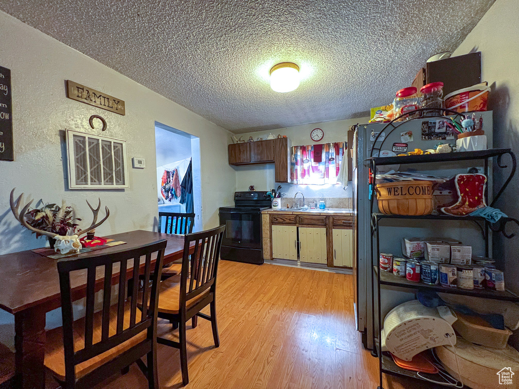 Kitchen featuring black appliances, sink, light wood-type flooring, and a textured ceiling