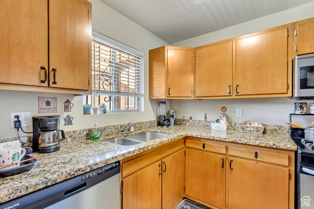 Kitchen with stainless steel appliances, light stone counters, and sink