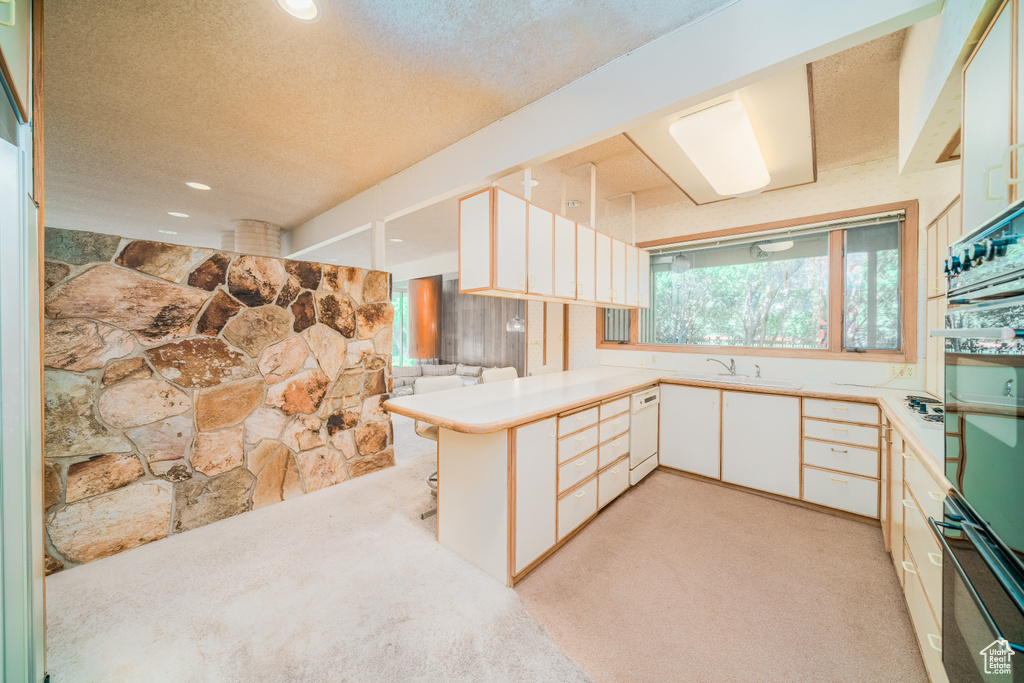 Kitchen with black oven, a textured ceiling, kitchen peninsula, light colored carpet, and sink