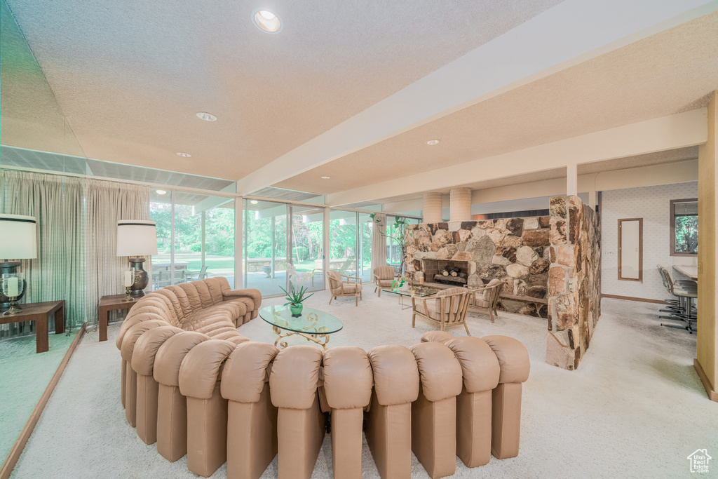 Living room with a stone fireplace, light carpet, a wall of windows, and a textured ceiling