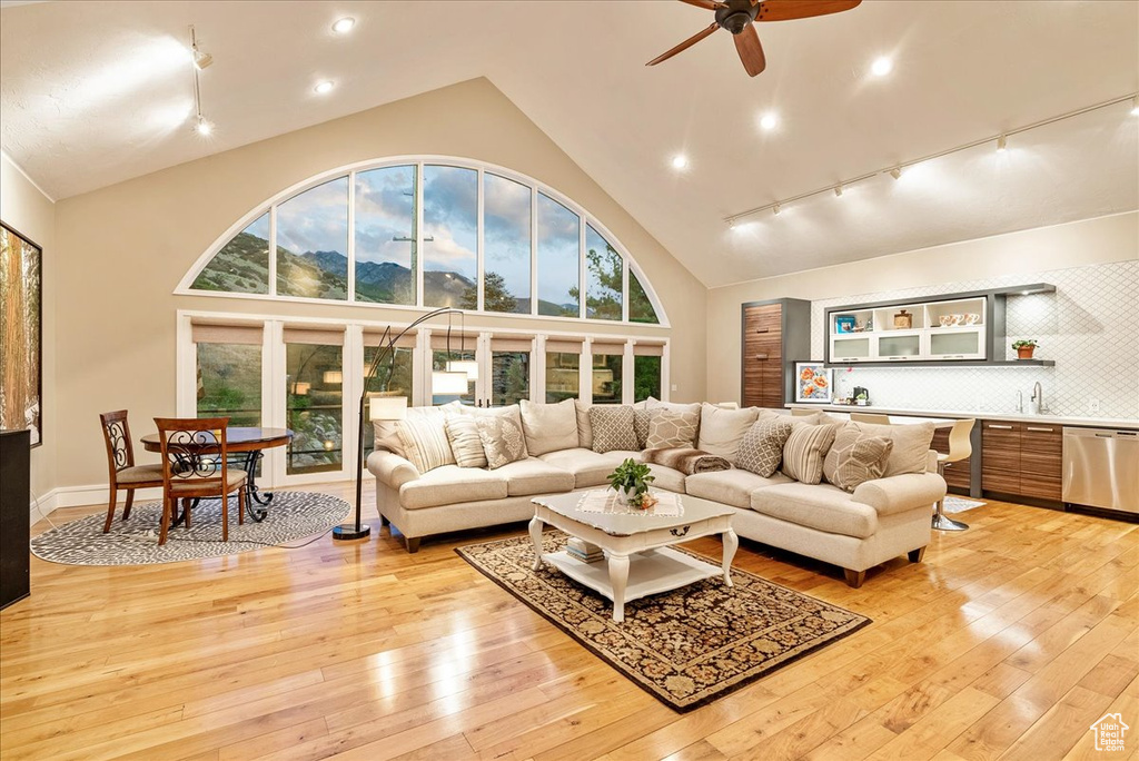 Living room with ceiling fan, rail lighting, high vaulted ceiling, light wood-type flooring, and sink