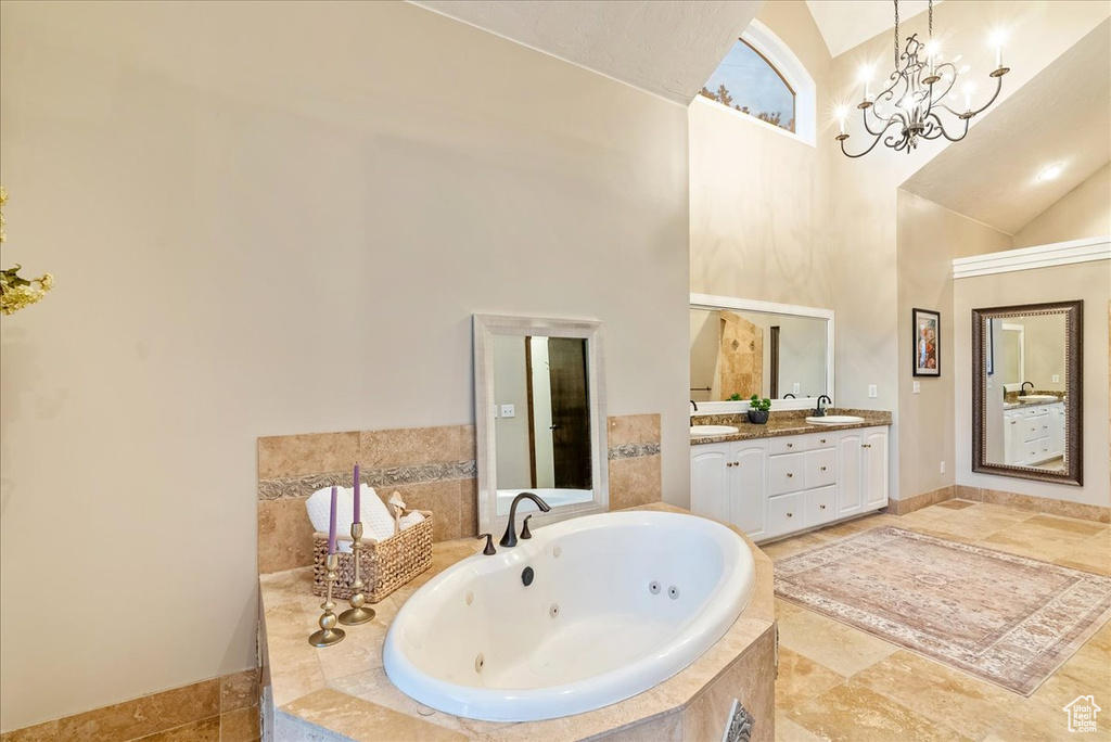 Bathroom with an inviting chandelier, dual bowl vanity, tiled bath, tile patterned floors, and high vaulted ceiling