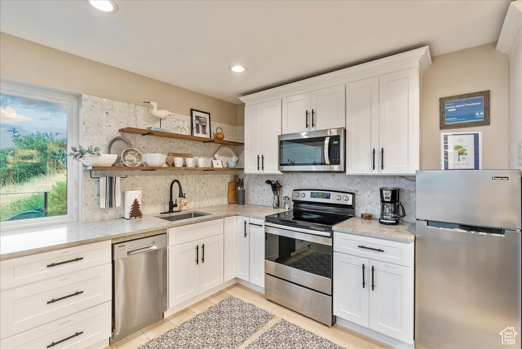 Kitchen featuring tasteful backsplash, white cabinets, light stone countertops, appliances with stainless steel finishes, and sink