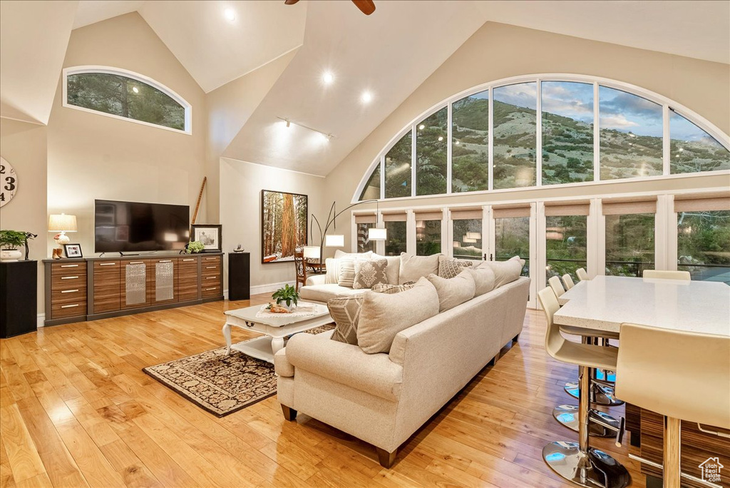 Living room featuring a wealth of natural light, light wood-type flooring, ceiling fan, and high vaulted ceiling