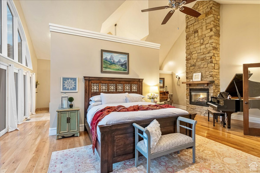 Bedroom with a stone fireplace, light hardwood / wood-style flooring, ceiling fan, and high vaulted ceiling