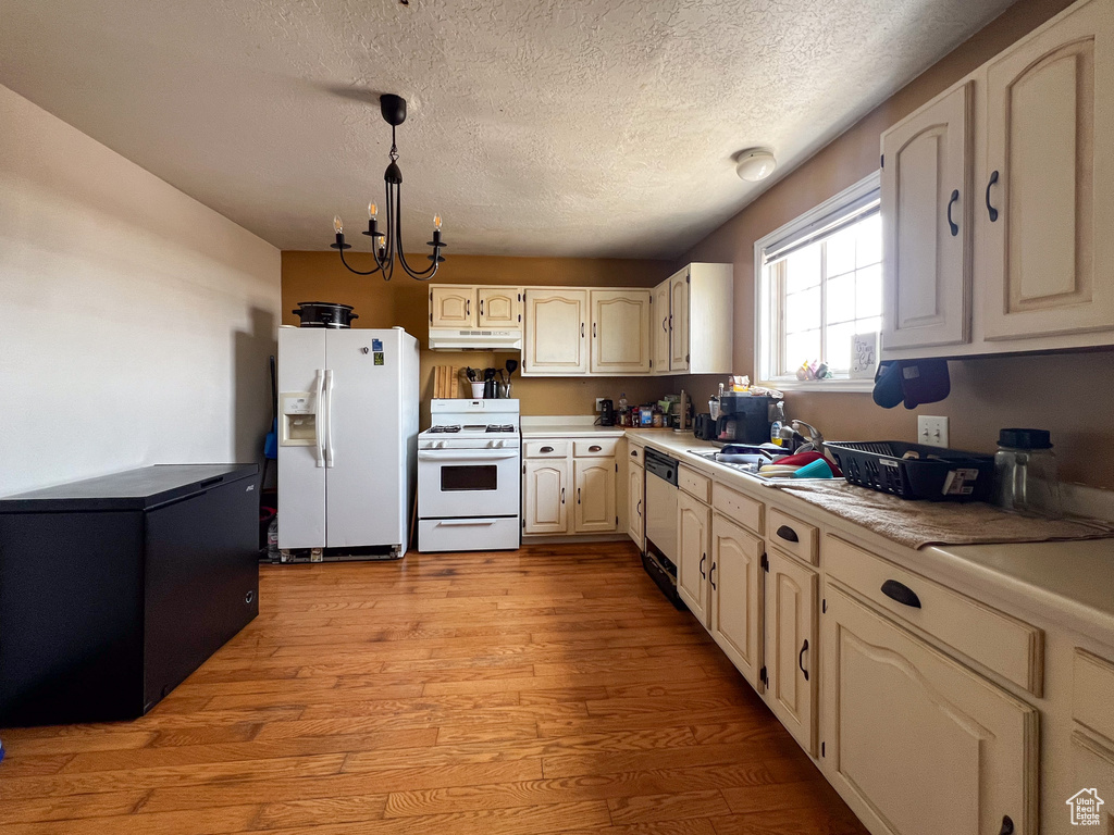 Kitchen with white appliances, an inviting chandelier, decorative light fixtures, light wood-type flooring, and a textured ceiling