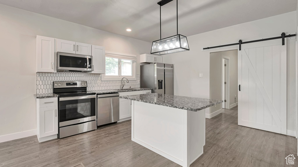 Kitchen with decorative backsplash, white cabinetry, stainless steel appliances, and a barn door