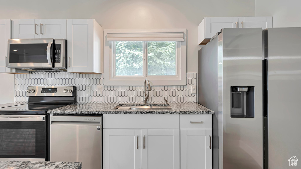 Kitchen featuring dark stone counters, tasteful backsplash, stainless steel appliances, and white cabinets