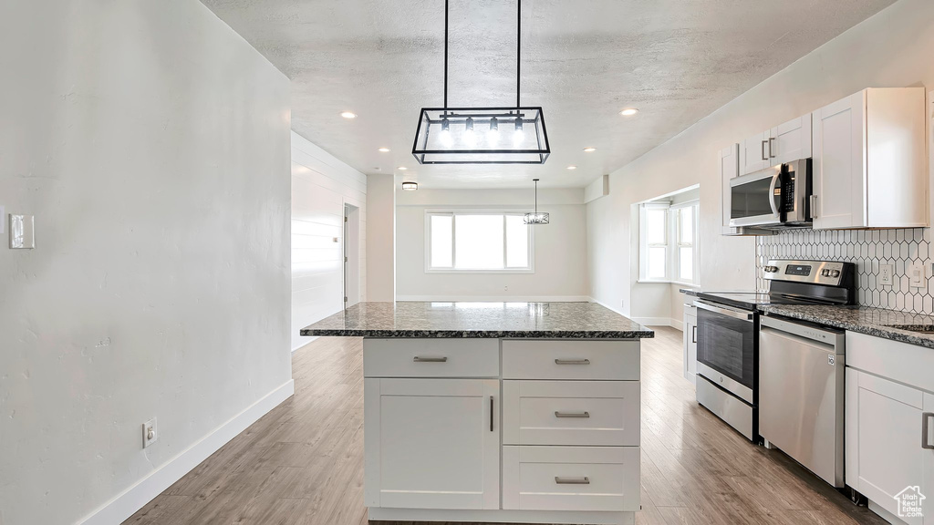 Kitchen featuring white cabinetry, stainless steel appliances, a center island, light hardwood / wood-style floors, and backsplash