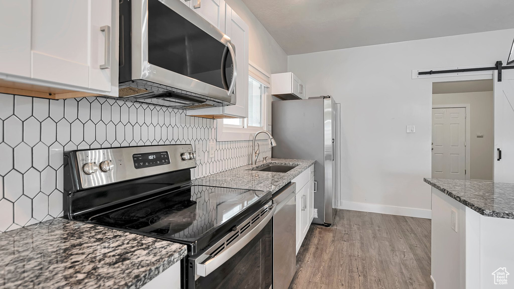 Kitchen featuring light hardwood / wood-style floors, white cabinets, backsplash, and stainless steel appliances