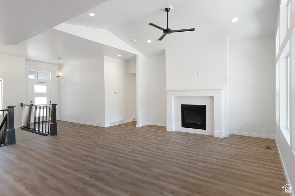 Unfurnished living room featuring high vaulted ceiling, ceiling fan, hardwood / wood-style floors, and a brick fireplace