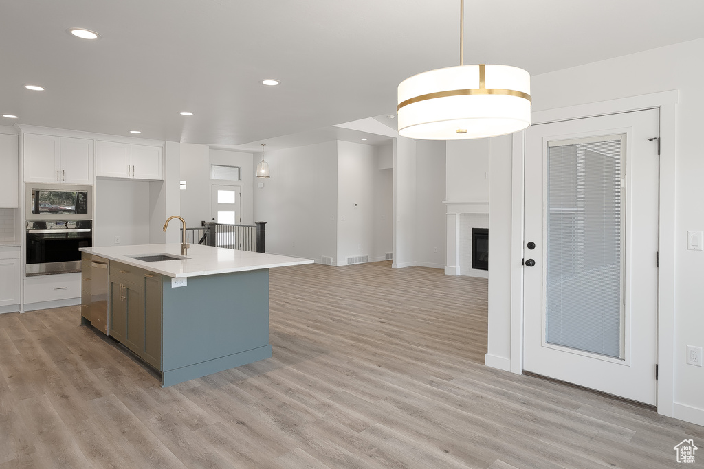 Kitchen with a kitchen island with sink, appliances with stainless steel finishes, sink, and light wood-type flooring