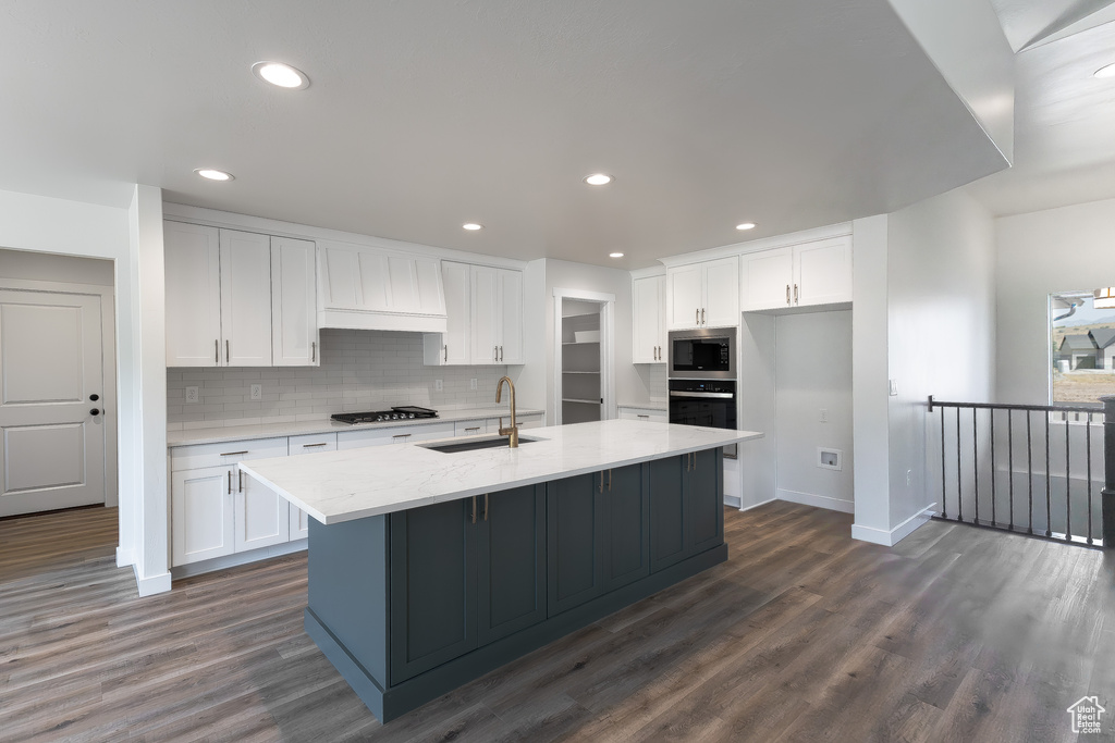 Kitchen with sink, white cabinetry, dark wood-type flooring, and an island with sink