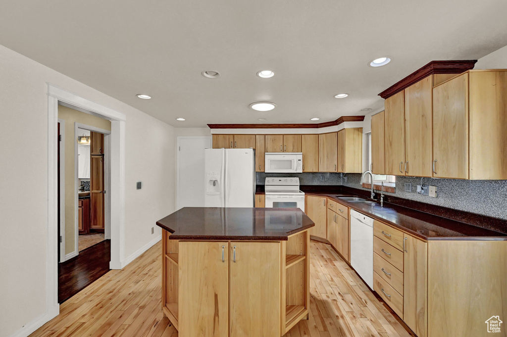 Kitchen featuring light brown cabinets, light wood-type flooring, white appliances, a center island, and sink