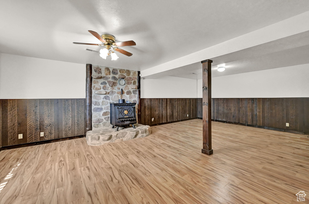 Unfurnished living room with a wood stove, light hardwood / wood-style floors, and ceiling fan