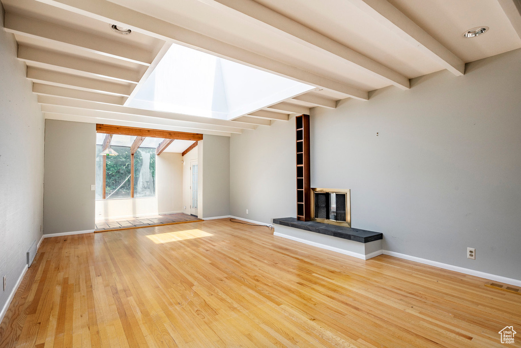 Unfurnished living room featuring beamed ceiling and light hardwood / wood-style flooring