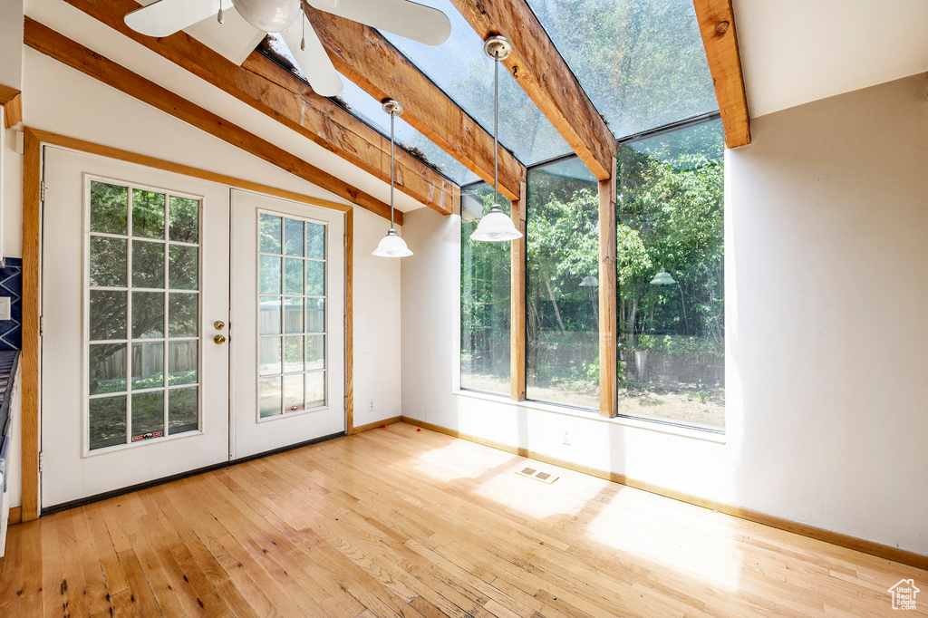 Unfurnished sunroom featuring vaulted ceiling with beams, a wealth of natural light, ceiling fan, and french doors