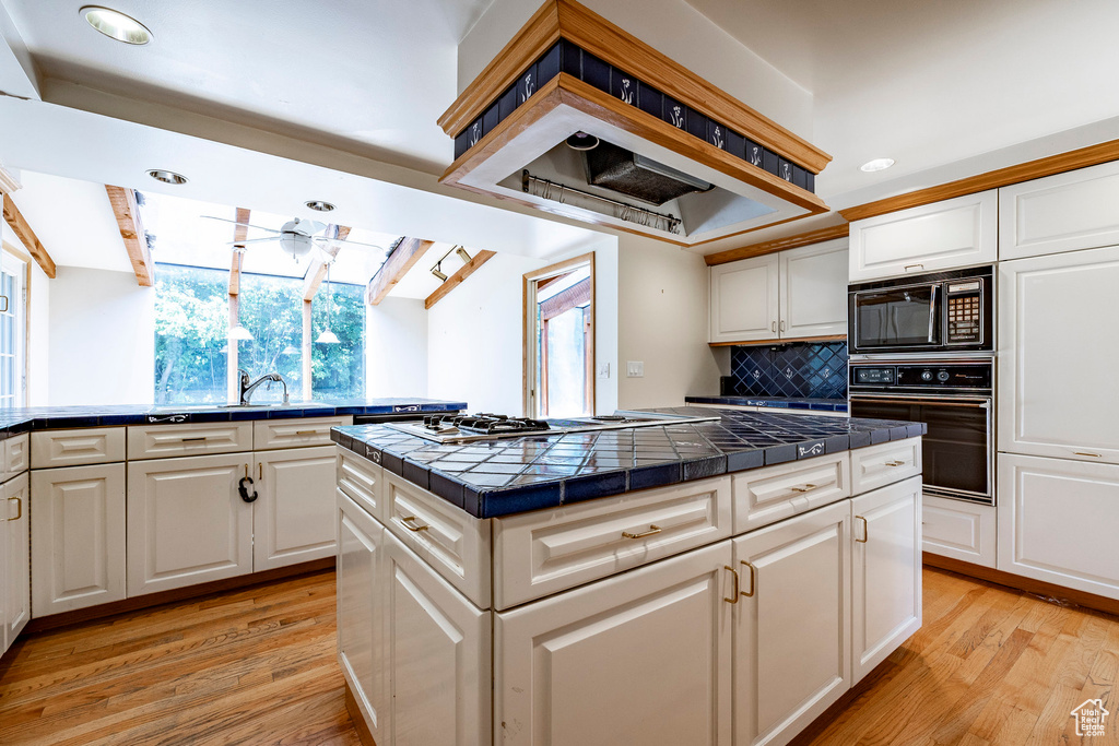 Kitchen featuring tasteful backsplash, white cabinets, light hardwood / wood-style floors, black appliances, and tile countertops