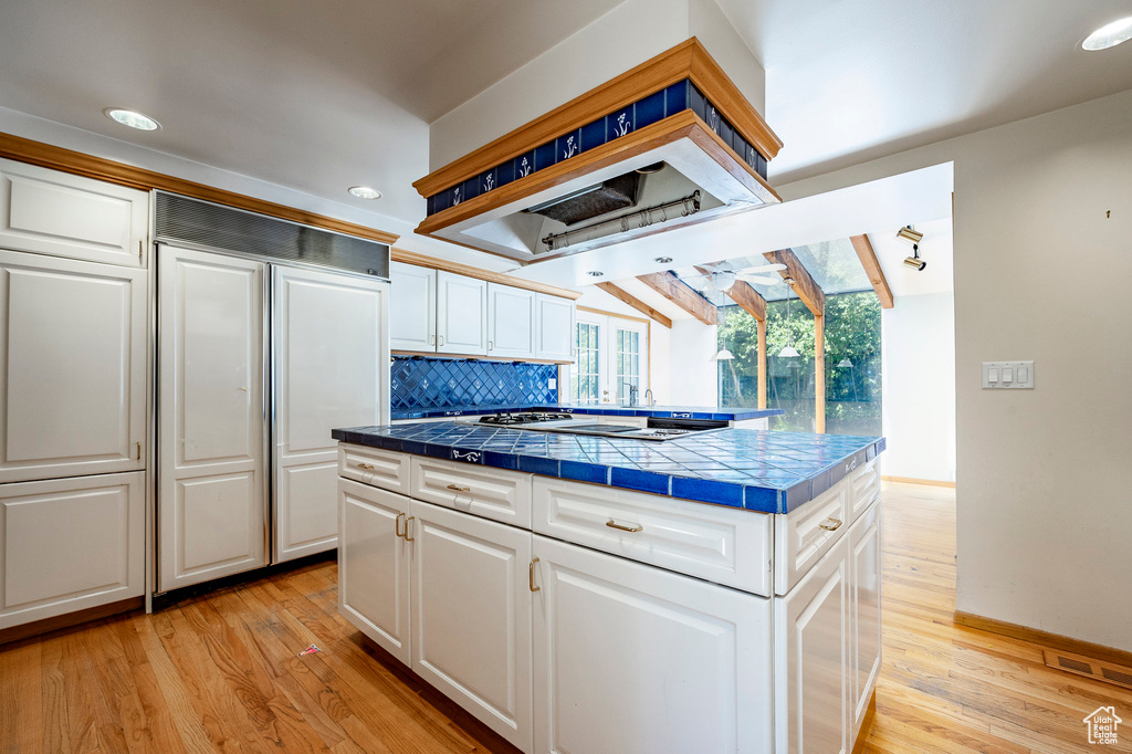 Kitchen with light hardwood / wood-style flooring, a kitchen island, decorative backsplash, tile counters, and white cabinetry