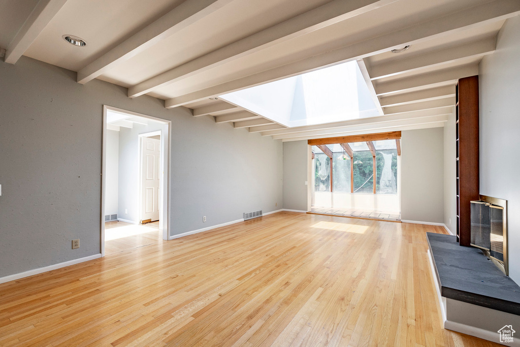 Unfurnished living room with beam ceiling and light wood-type flooring