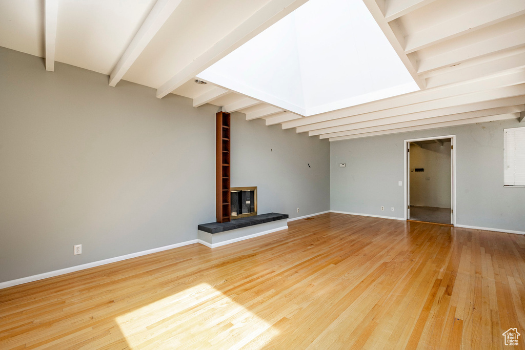 Unfurnished living room featuring a tile fireplace, beamed ceiling, and light hardwood / wood-style flooring