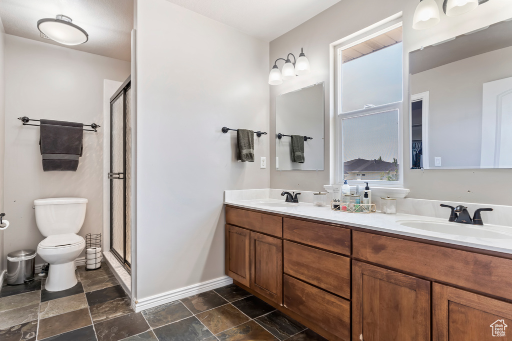 Bathroom with a shower with shower door, tile patterned floors, double sink vanity, and toilet