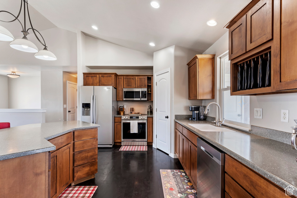 Kitchen featuring dark wood-type flooring, appliances with stainless steel finishes, pendant lighting, vaulted ceiling, and sink