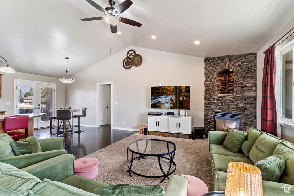 Living room with french doors, dark hardwood / wood-style flooring, ceiling fan, a stone fireplace, and vaulted ceiling