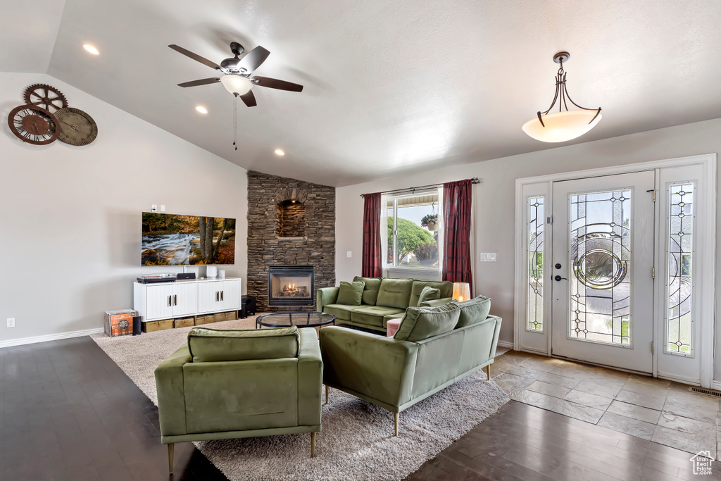 Living room with a stone fireplace, lofted ceiling, light hardwood / wood-style flooring, and ceiling fan