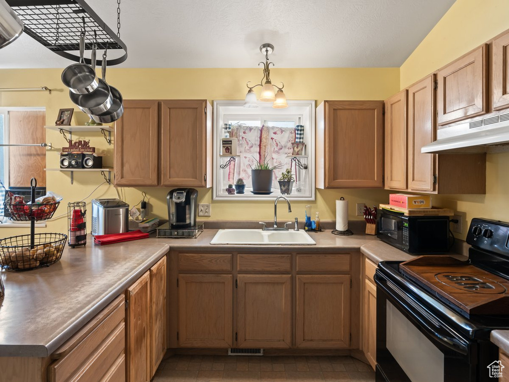 Kitchen featuring dark tile patterned flooring, black appliances, hanging light fixtures, and sink