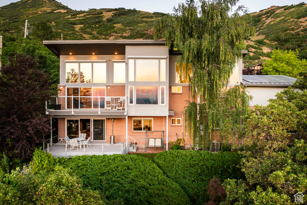 Rear view of house with a balcony, a patio area, central AC, and a mountain view