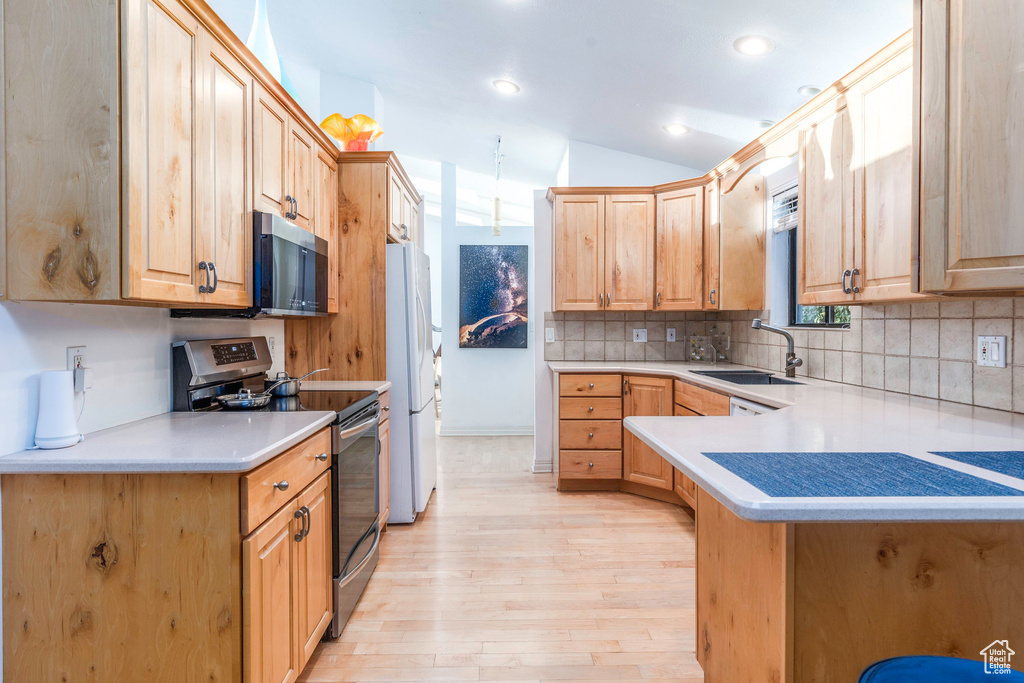 Kitchen featuring tasteful backsplash, sink, appliances with stainless steel finishes, light hardwood / wood-style flooring, and lofted ceiling