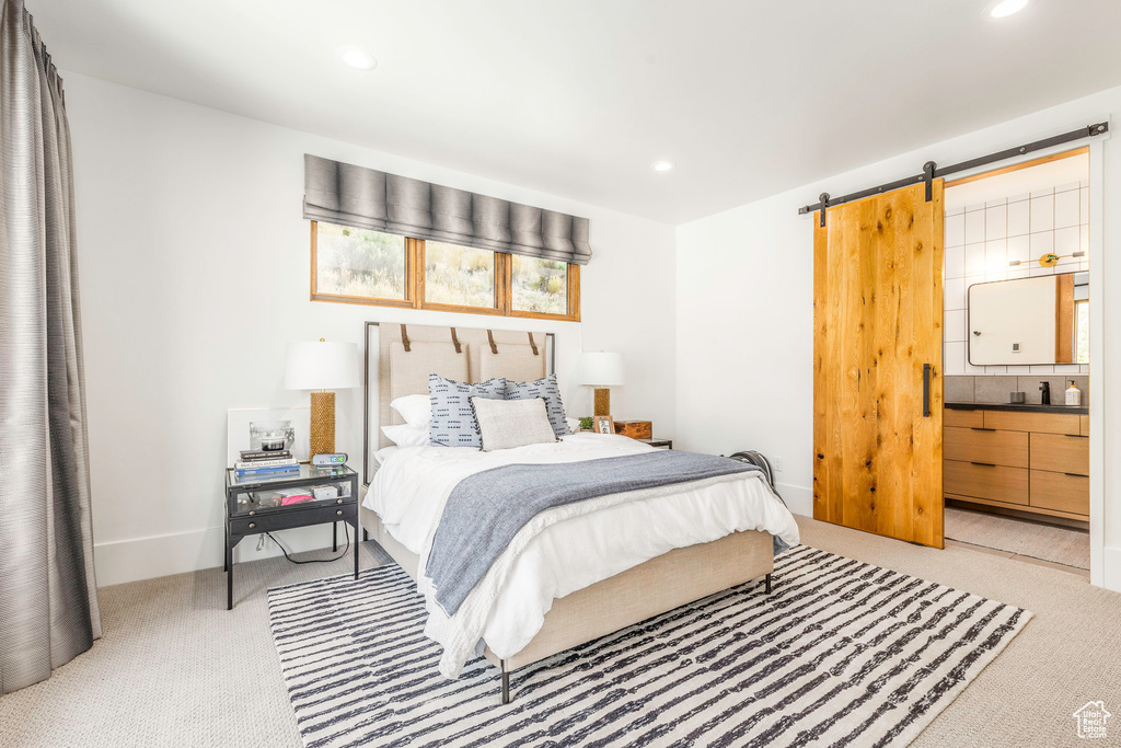 Bedroom featuring ensuite bath, light carpet, and a barn door