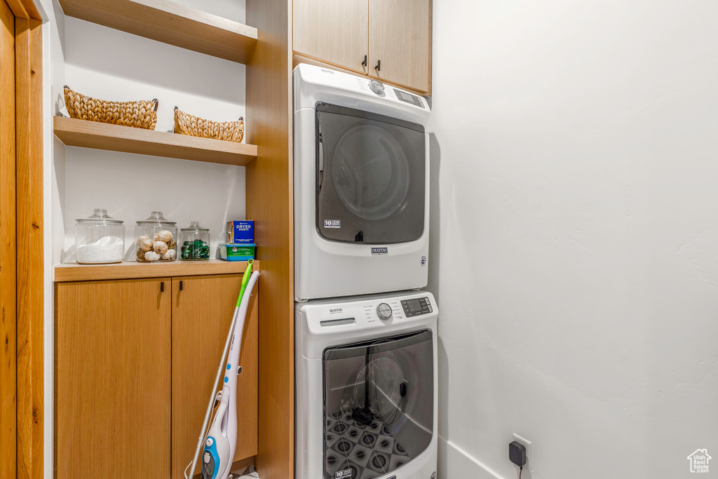 Laundry area featuring stacked washer / dryer and cabinets