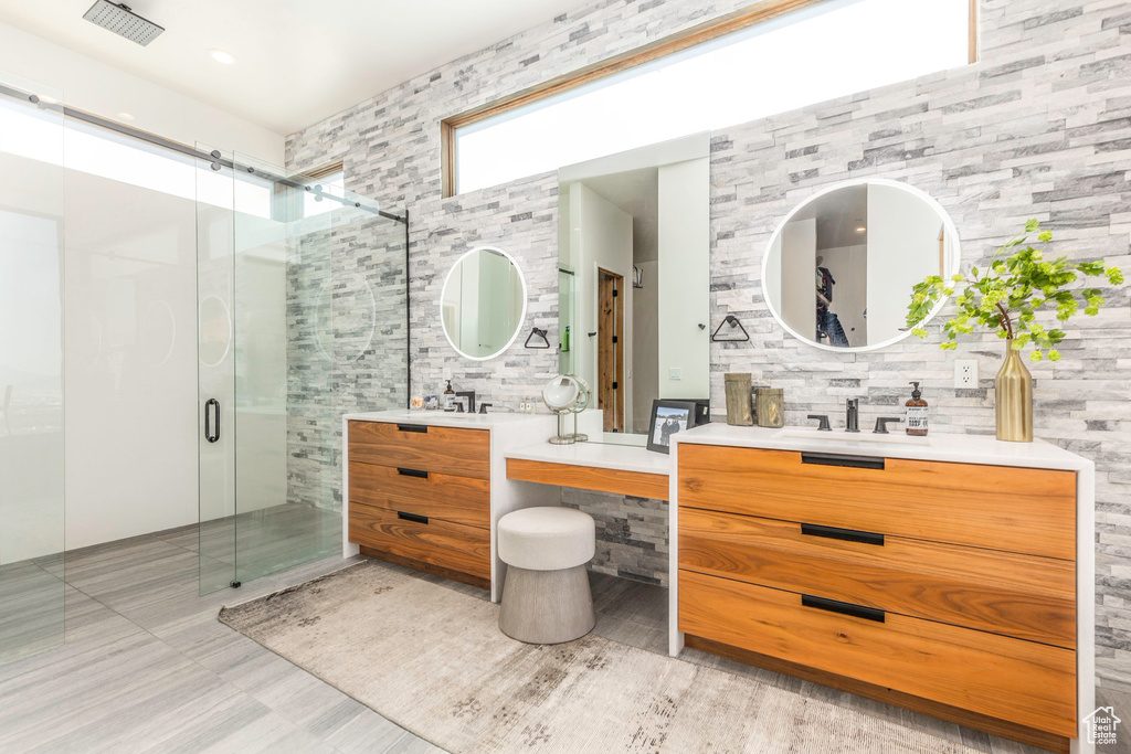 Bathroom with dual vanity, a shower with door, tile patterned flooring, and tile walls